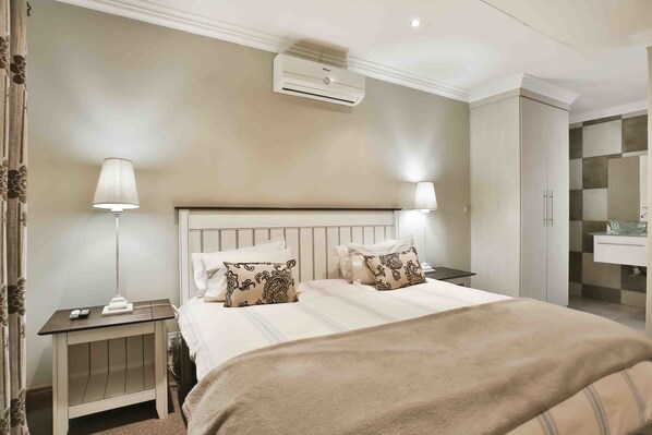 A hotel room with a bed, bedside tables, a lamp, an air conditioner, and a bathroom with a sink and mirror. - Accommodation @ Van's (Centurion)