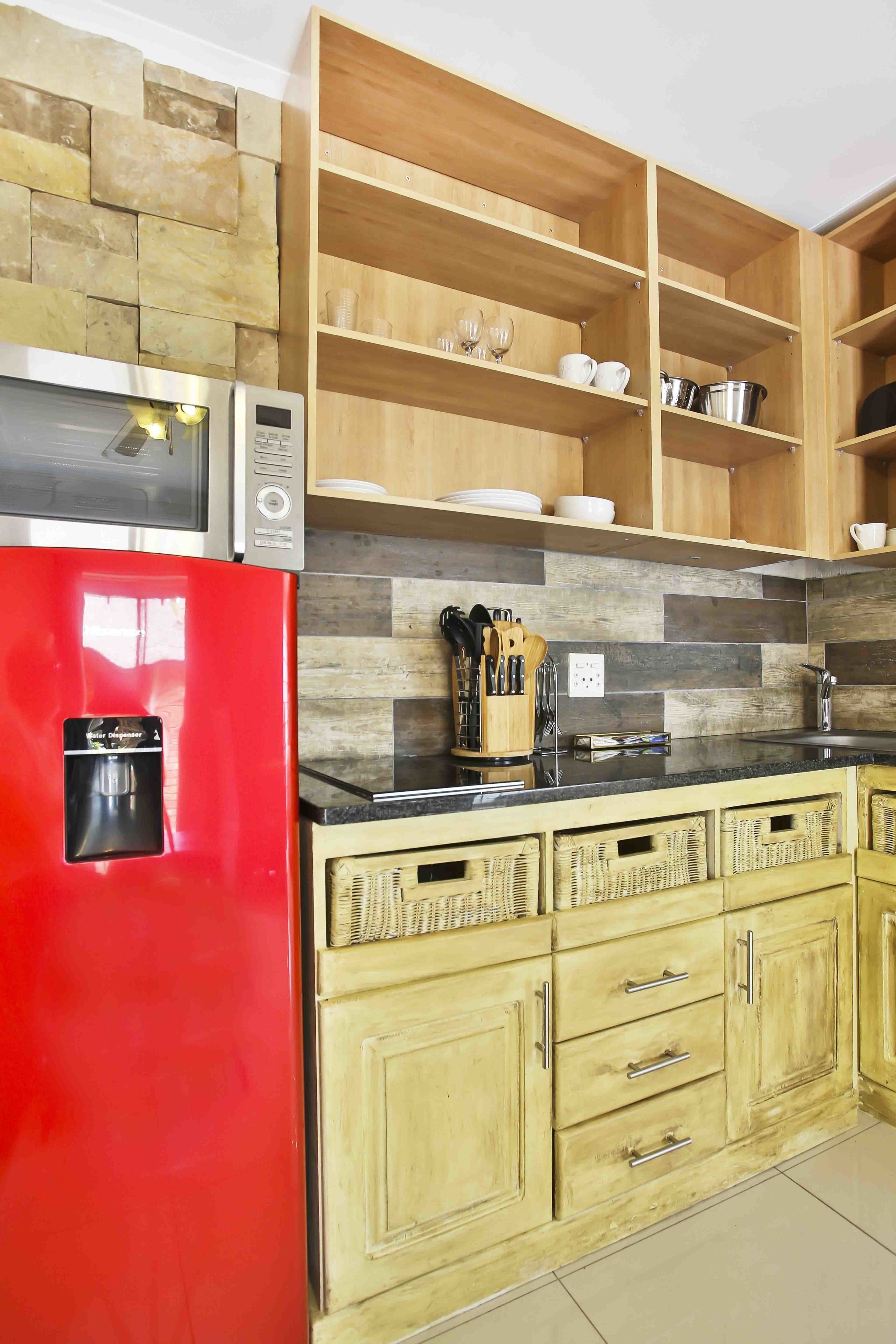 A kitchen with a red refrigerator, wooden cabinets, and a tiled backsplash.