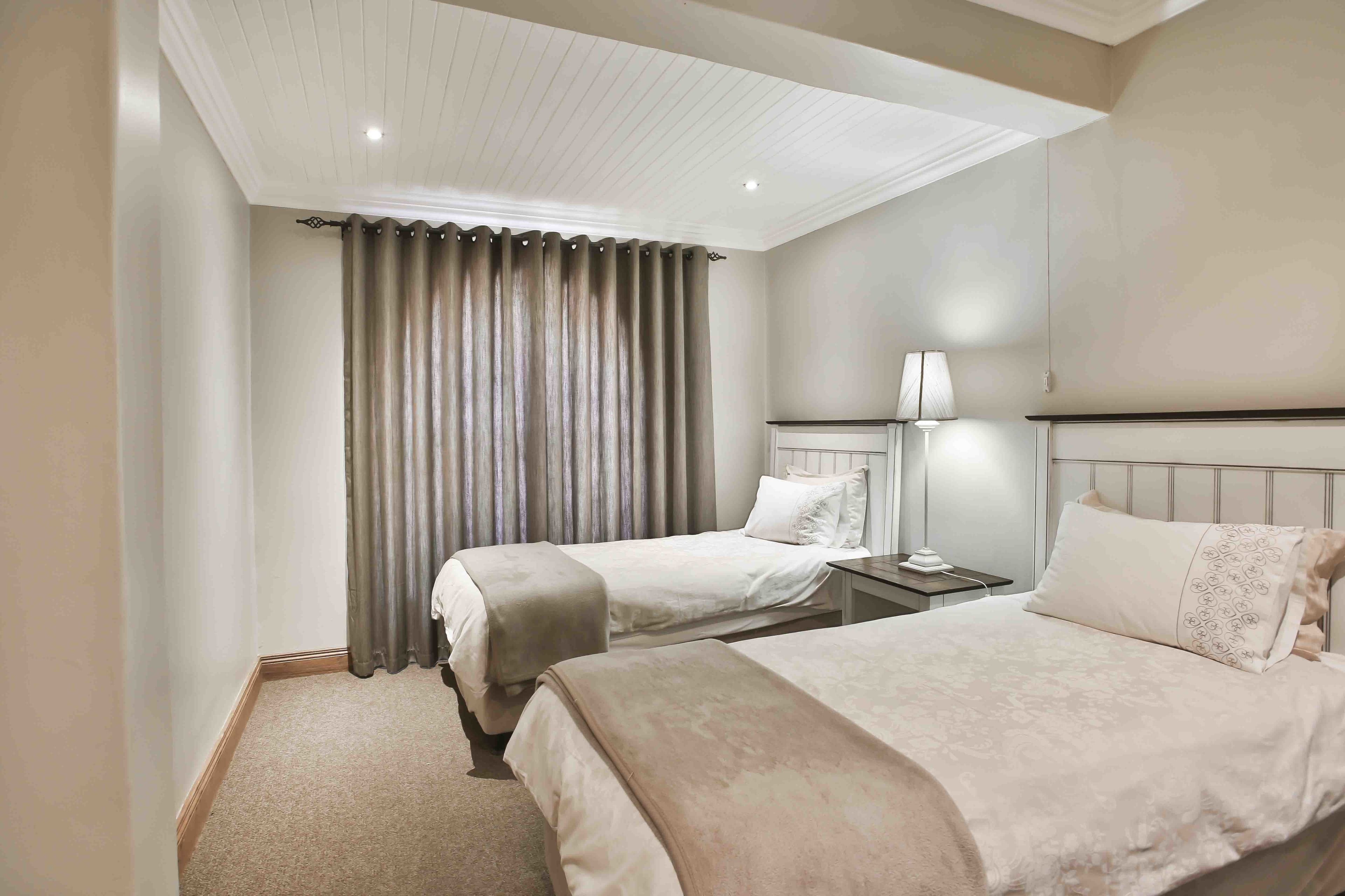 Een hotelkamer met twee bedden, een nachtkastje, een lamp en een plafond met inbouwspots.