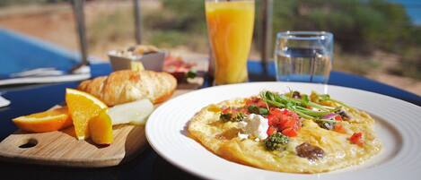 A breakfast setting with a plate of food, a glass of orange juice, and a water glass on a table with a view of the ocean.