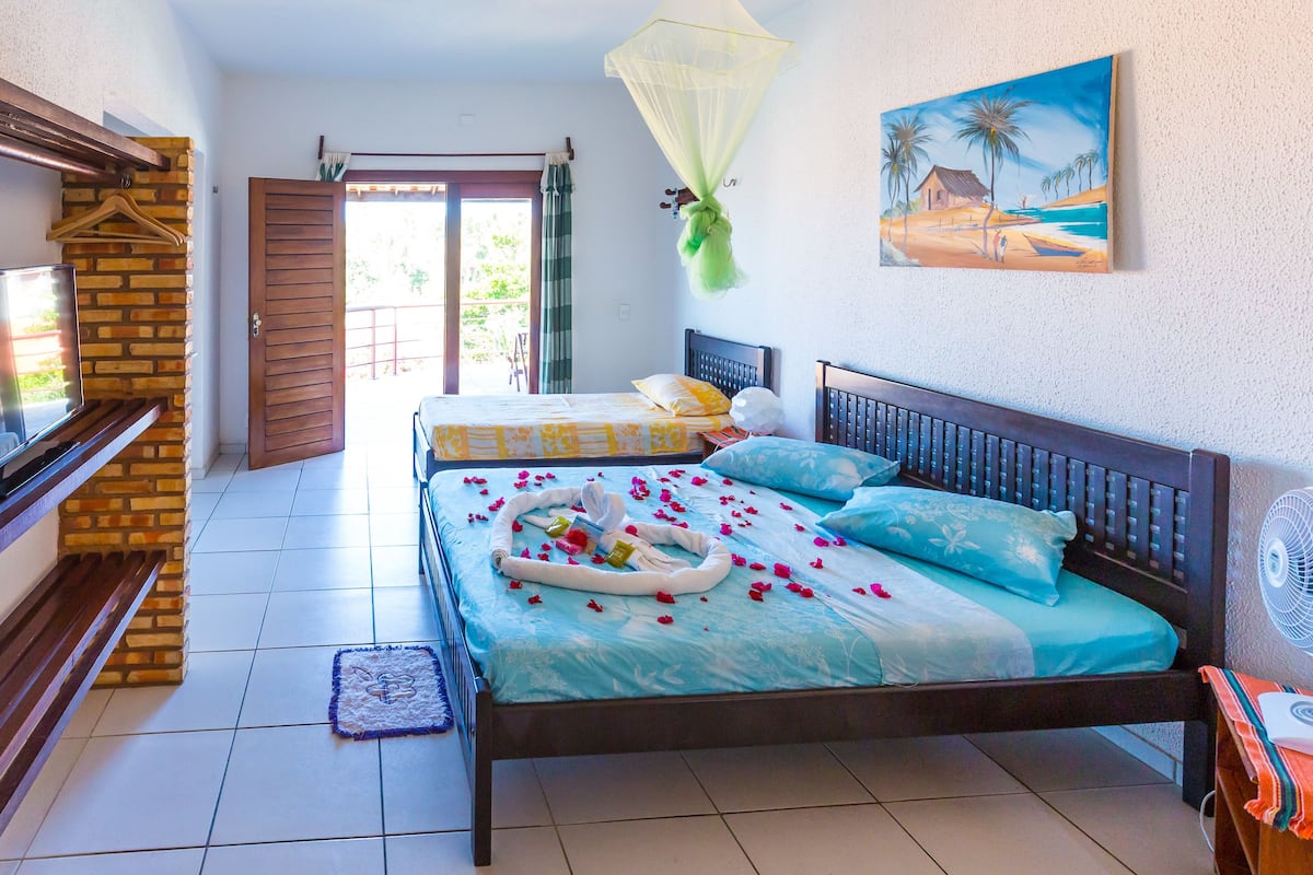 Una habitación con cama, banco, televisor y puerta.