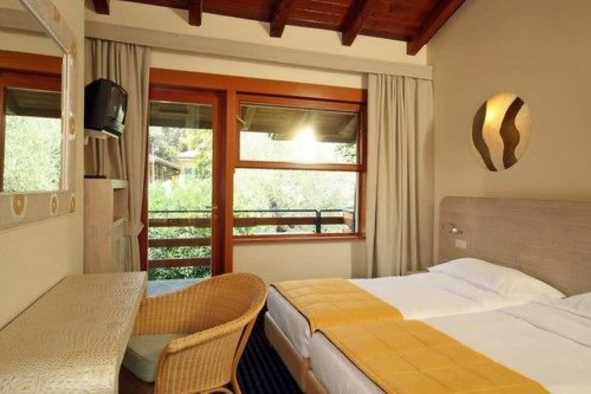A hotel room with a bed, a small table, a chair, a television, and a window with curtains.