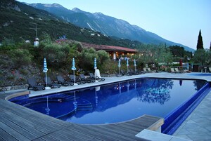 A swimming pool with lounge chairs and umbrellas, surrounded by mountains and a building with lights.