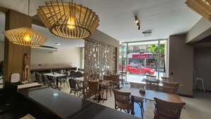 Un restaurante con un interior moderno, que presenta una zona de comedor central con mesas y sillas, una pared decorativa con diseños recortados y lámparas colgantes.