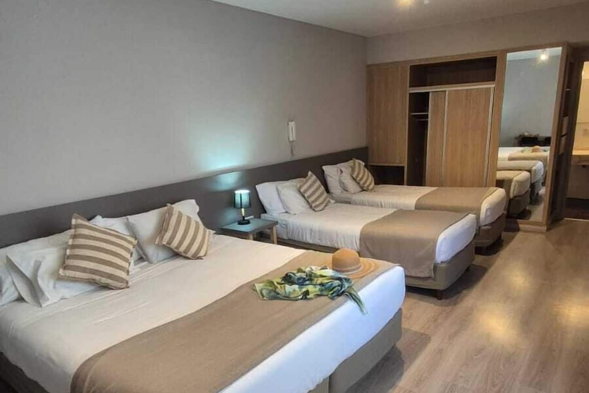 A hotel room with two beds, a wooden floor, a nightstand with a lamp, and a wardrobe.