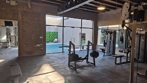 Un gimnasio con equipo de levantamiento de pesas, ventanas amplias y vistas a un espacio exterior.