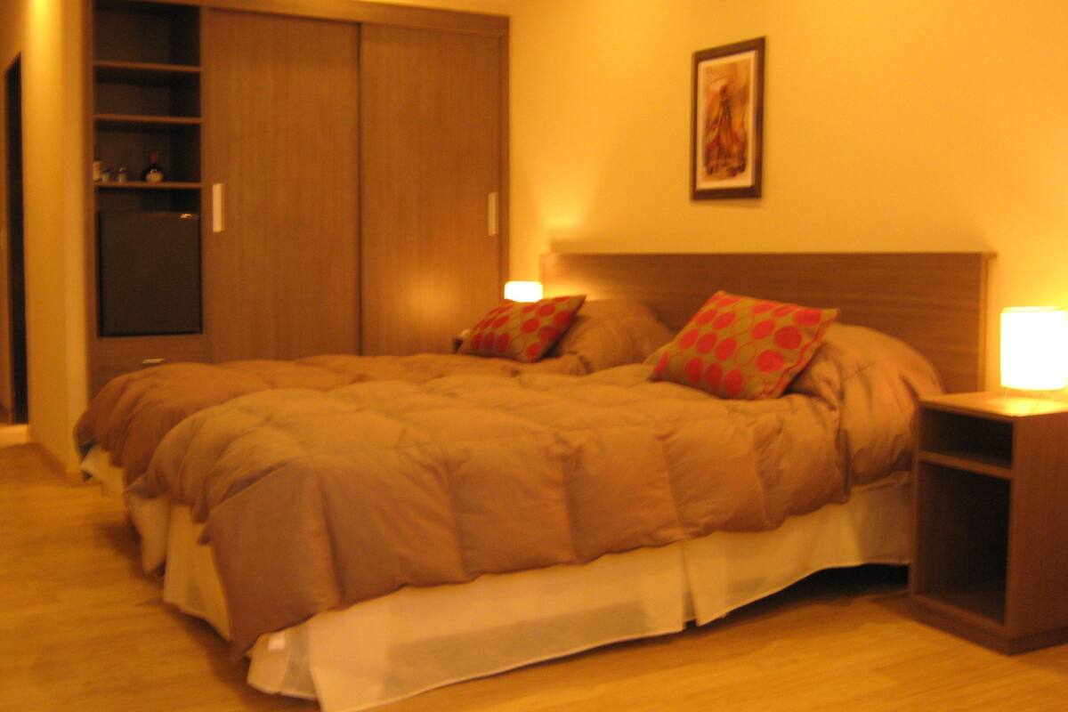 A bedroom with a bed, pillows, a nightstand, a wall-mounted picture, and a wardrobe.