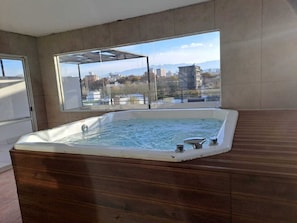 Un jacuzzi en una habitación con ventanas amplias con vistas a la ciudad.