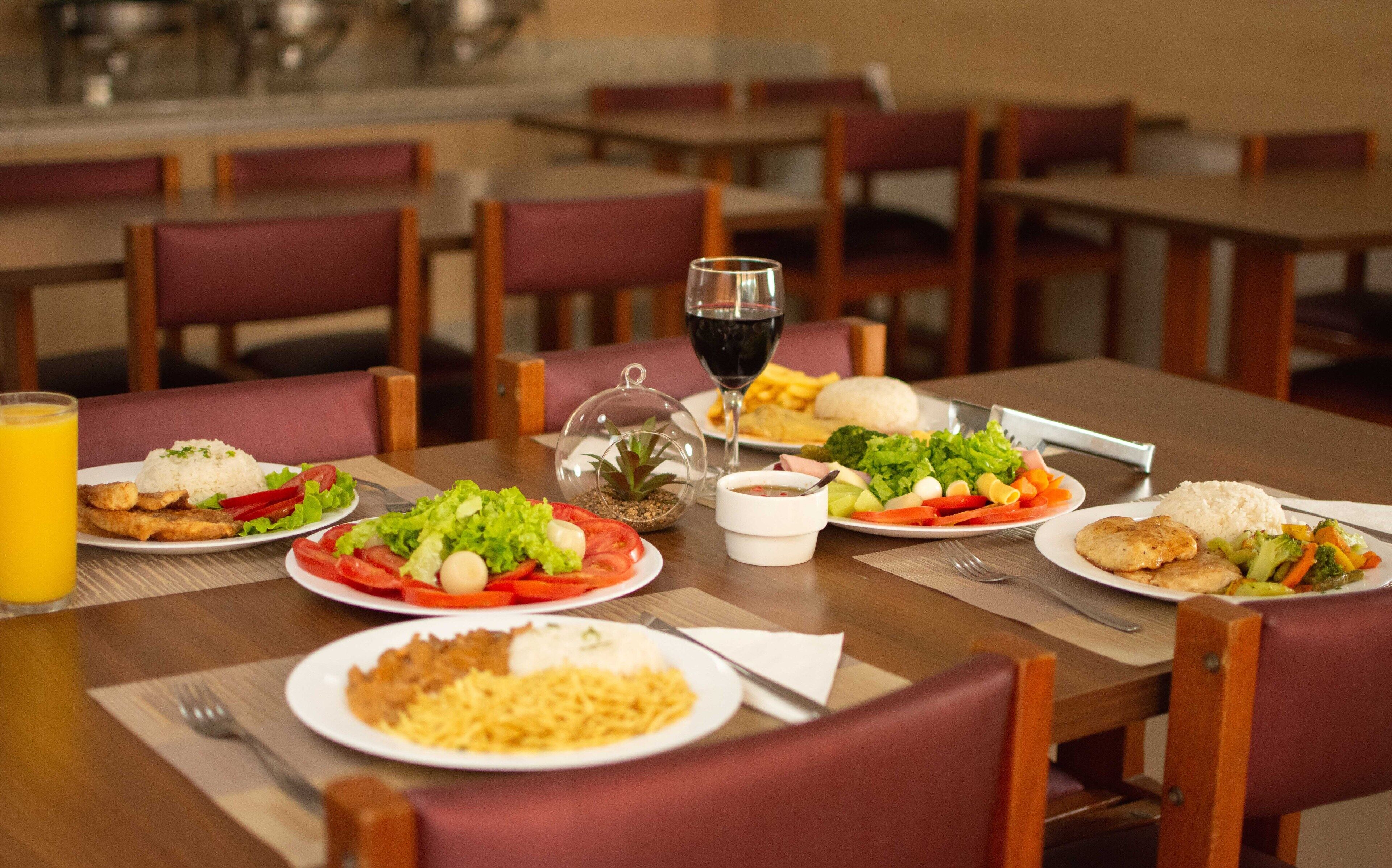 Una mesa de comedor con varios platos de comida, una copa de vino tinto y una pequeña planta.