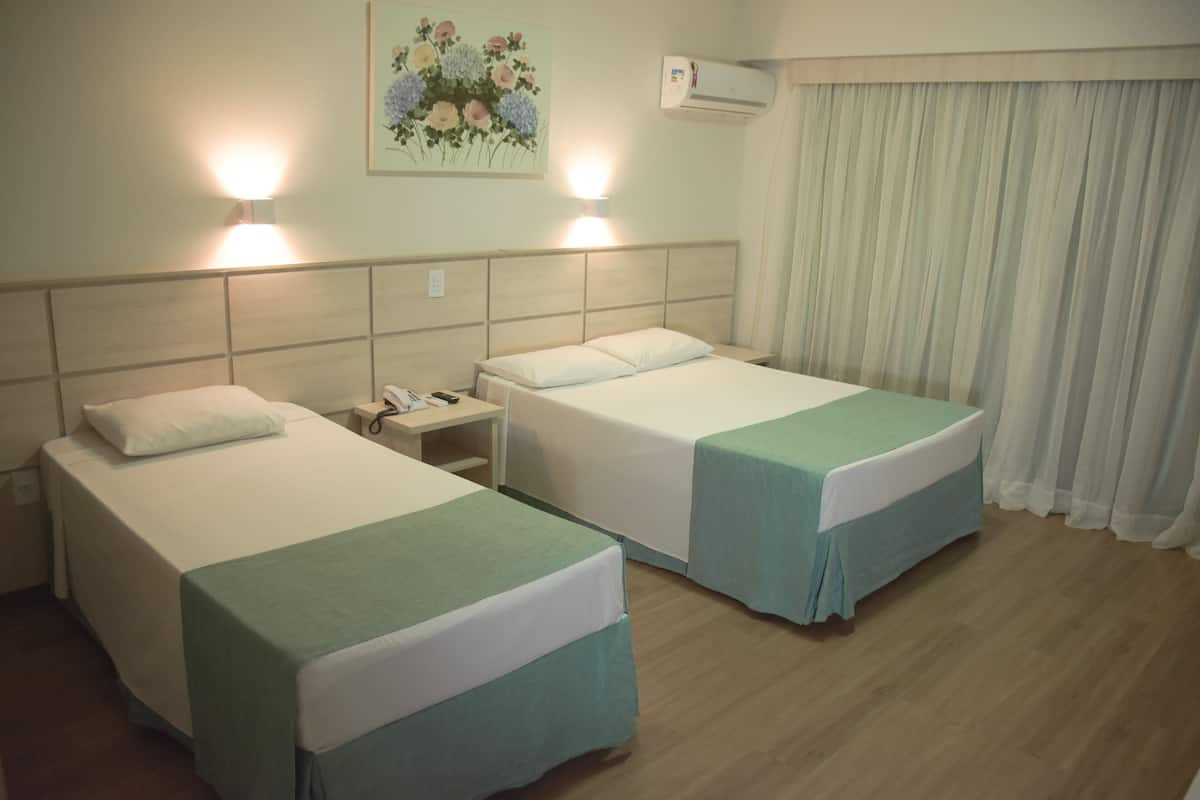 A hotel room with two beds, a nightstand, a telephone, and a wall-mounted air conditioner.