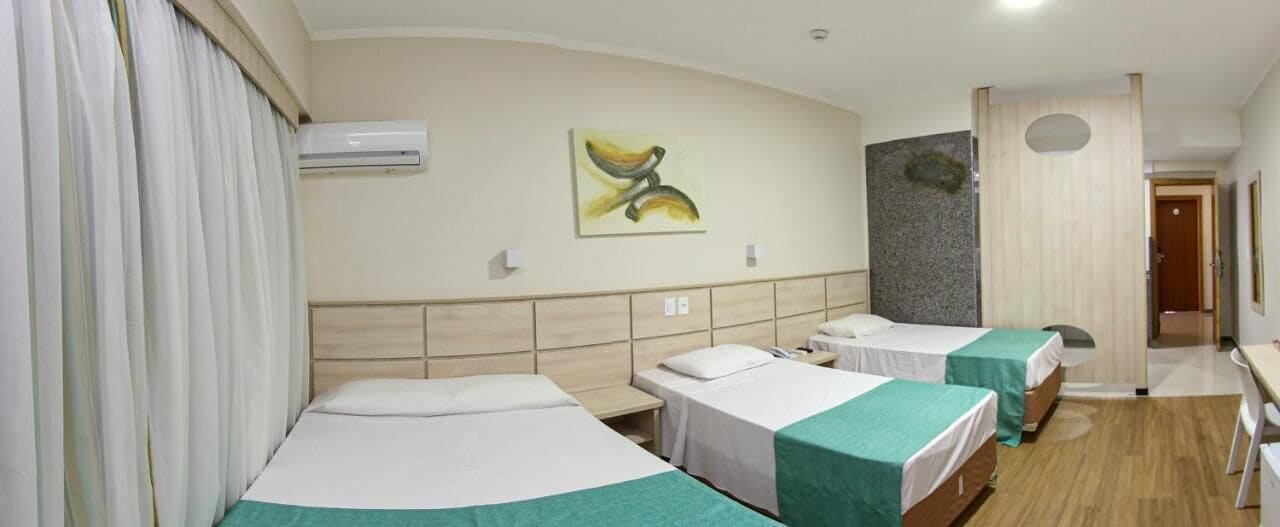 Habitación de hotel con tres camas, un cuadro en la pared, un equipo de aire acondicionado y piso de madera.