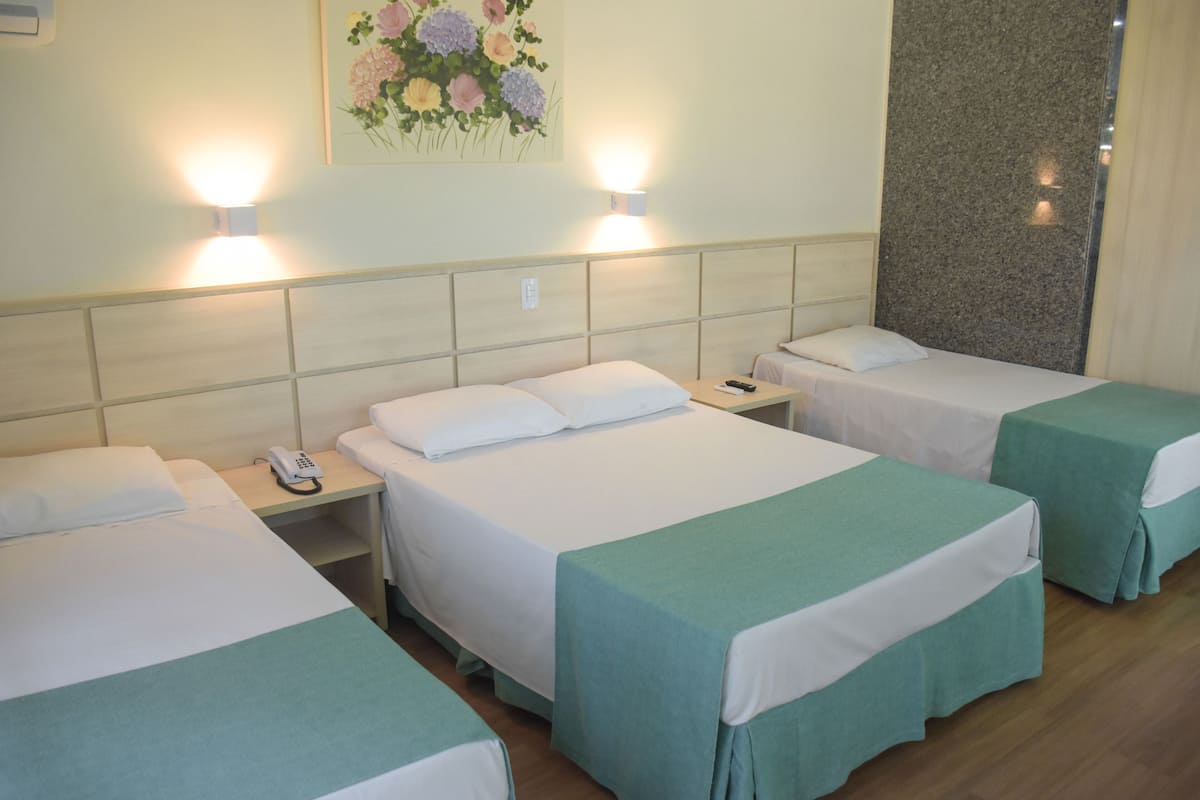 A hotel room with three beds, each with a green bedspread, white linens, and a bedside table with a phone.