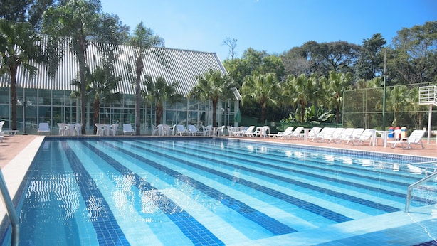A swimming pool with clear blue tiles, surrounded by white lounge chairs and palm trees.