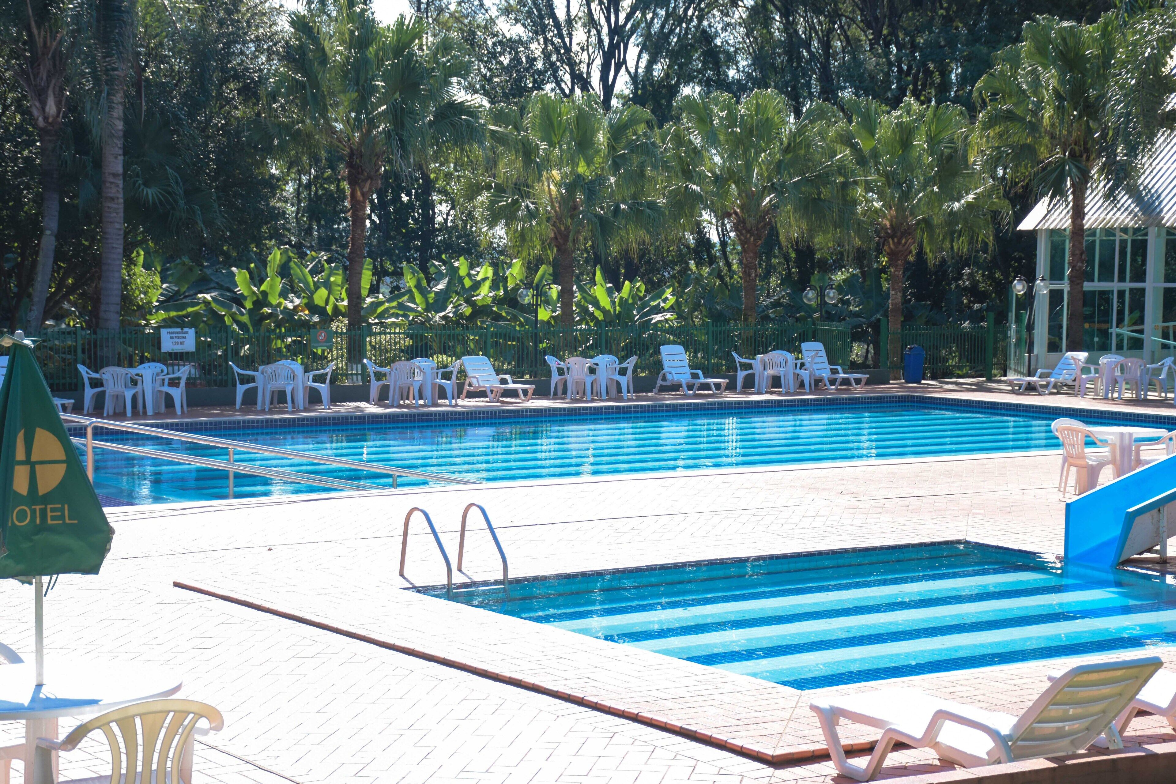 A swimming pool with lounge chairs and umbrellas, surrounded by palm trees and a fence.