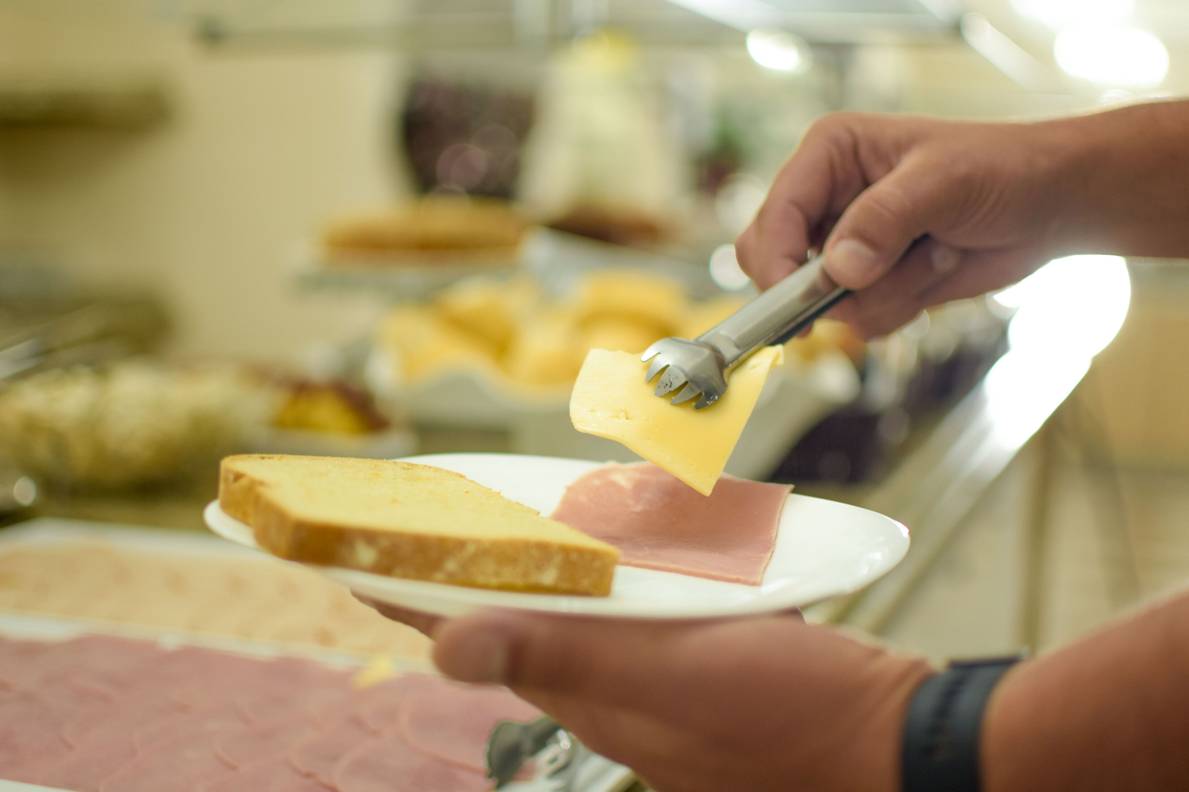 A person using a cheese slicer to cut cheese on a plate.