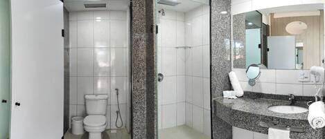 Un baño moderno con ducha envuelta en cristal, inodoro blanco y lavamanos de granito con espejo y toallero.