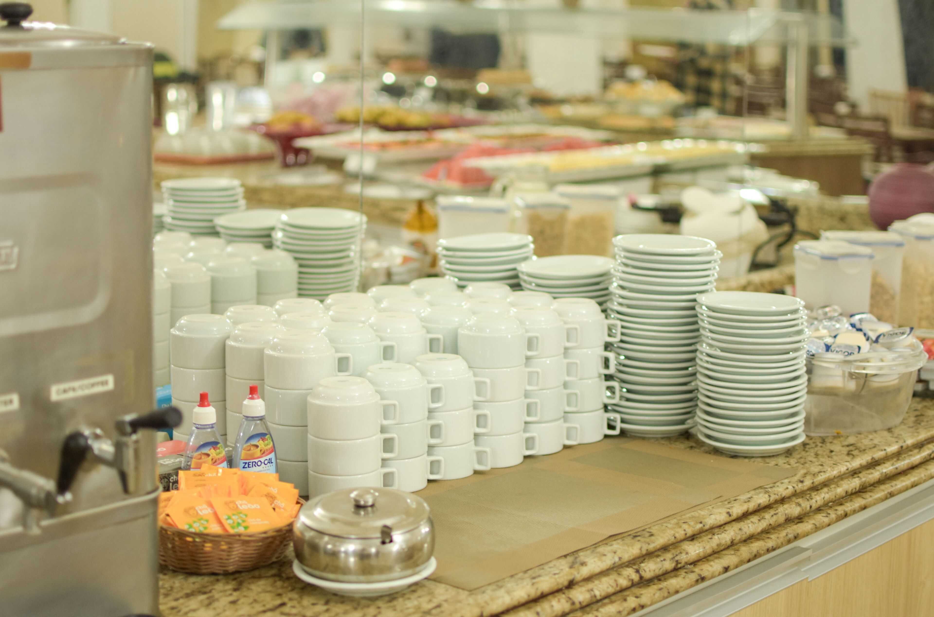 A buffet setup with stacks of white plates, bowls, and various food containers.