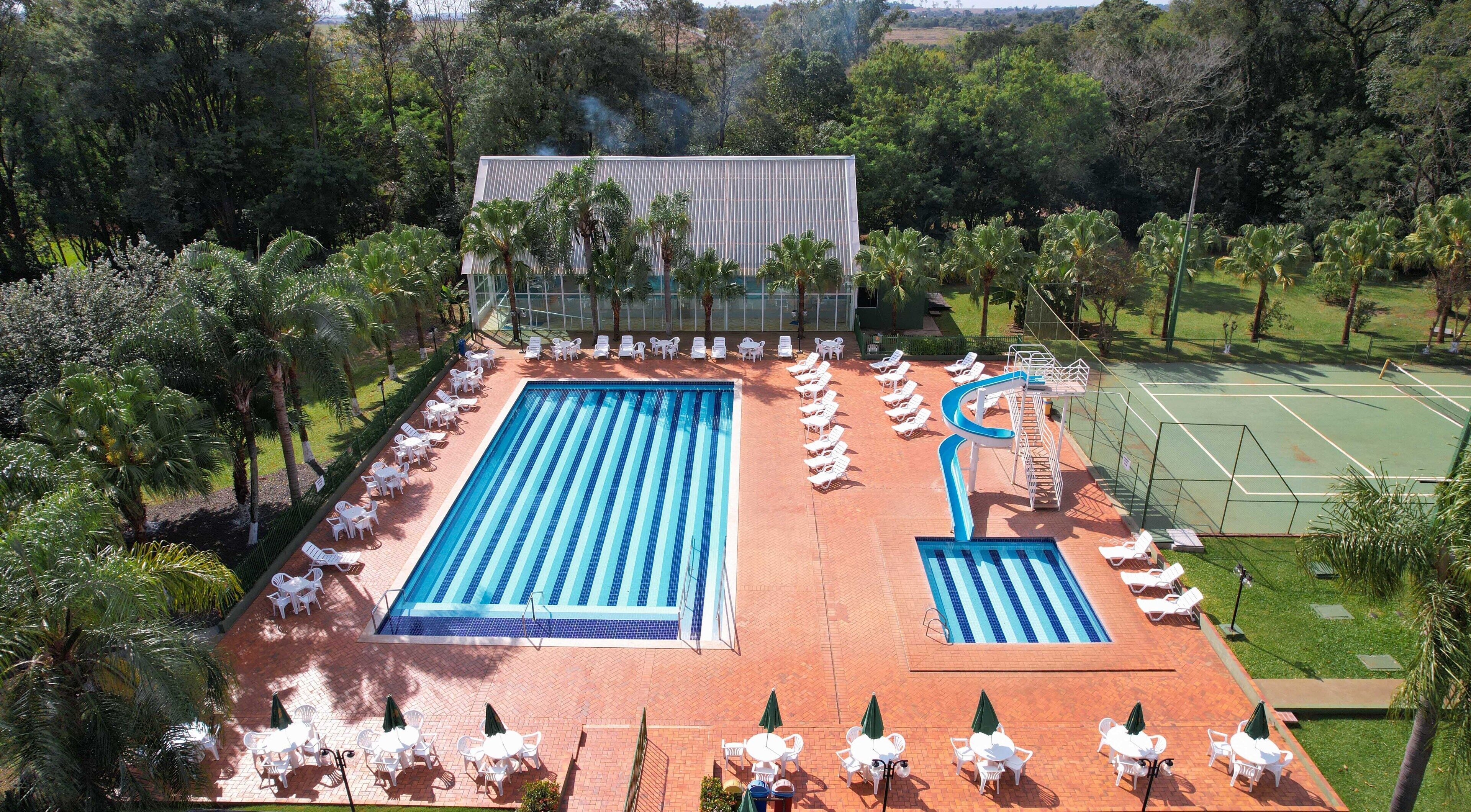 A swimming pool with adjacent lounge chairs and a tennis court.
