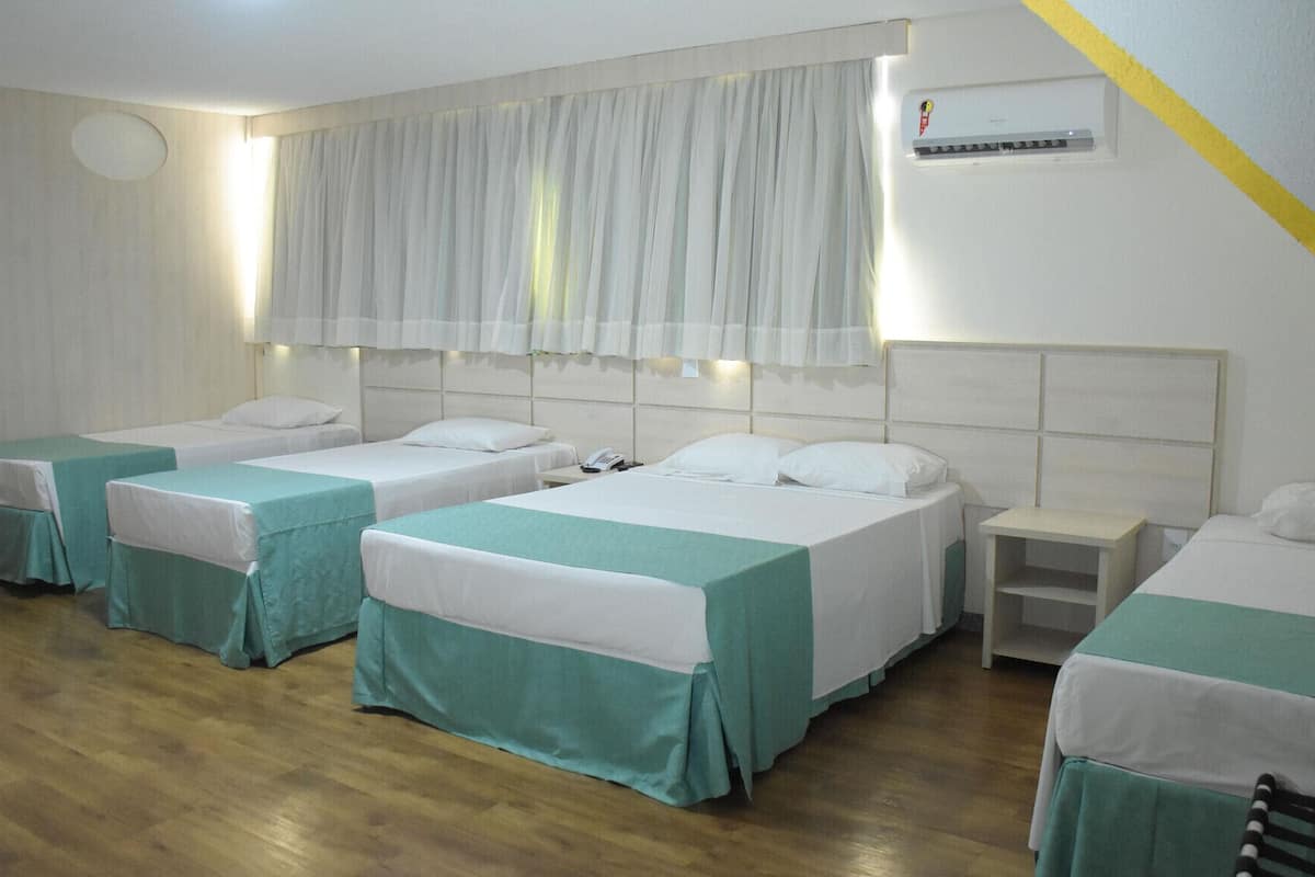 A hotel room with four single beds, a small bedside table with a phone, a wall-mounted air conditioner, and a window with sheer curtains.