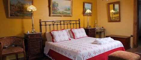Une chambre à coucher comprenant un lit, deux tables de chevet, une chaise, une commode en bois, un miroir et un lustre.