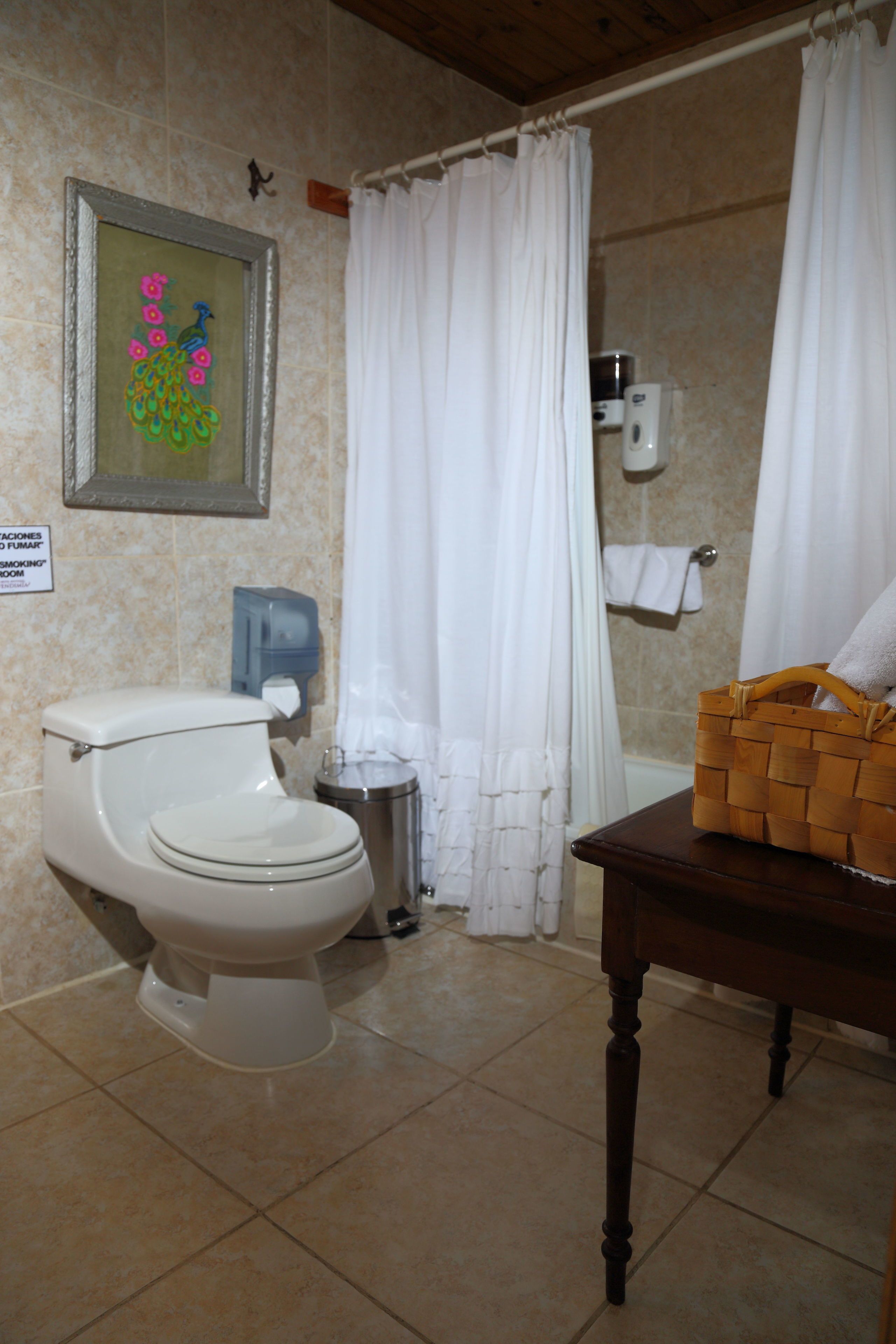 A bathroom with a toilet, a trash can, a basket on a table, and a shower curtain.