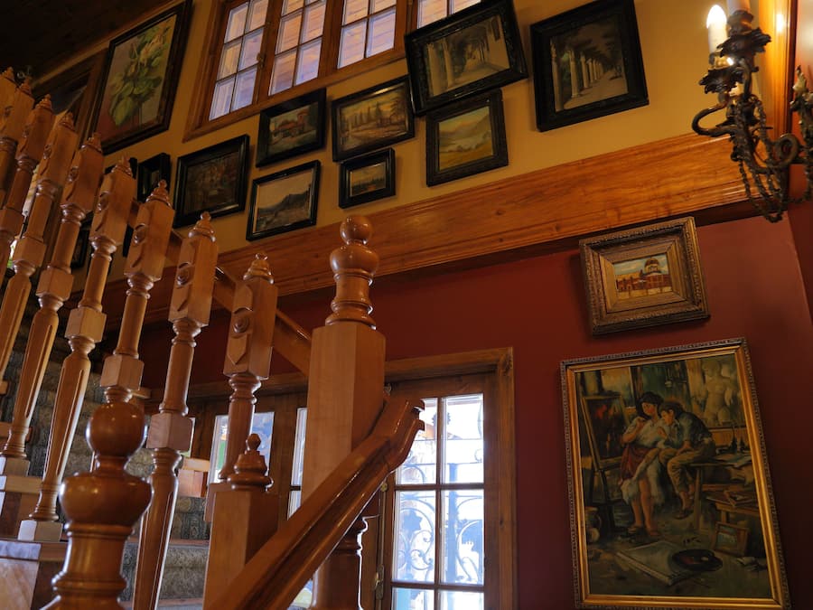 Una escalera con balaustres de madera, un cuadro con la imagen de dos personas y varias fotografías enmarcadas en la pared.