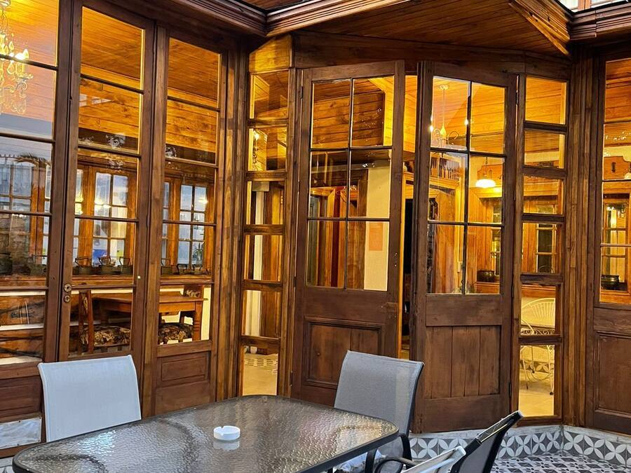 Un espacio de estar al aire libre cubierto con mesa y sillas de vidrio, paneles de madera y vistas al interior.