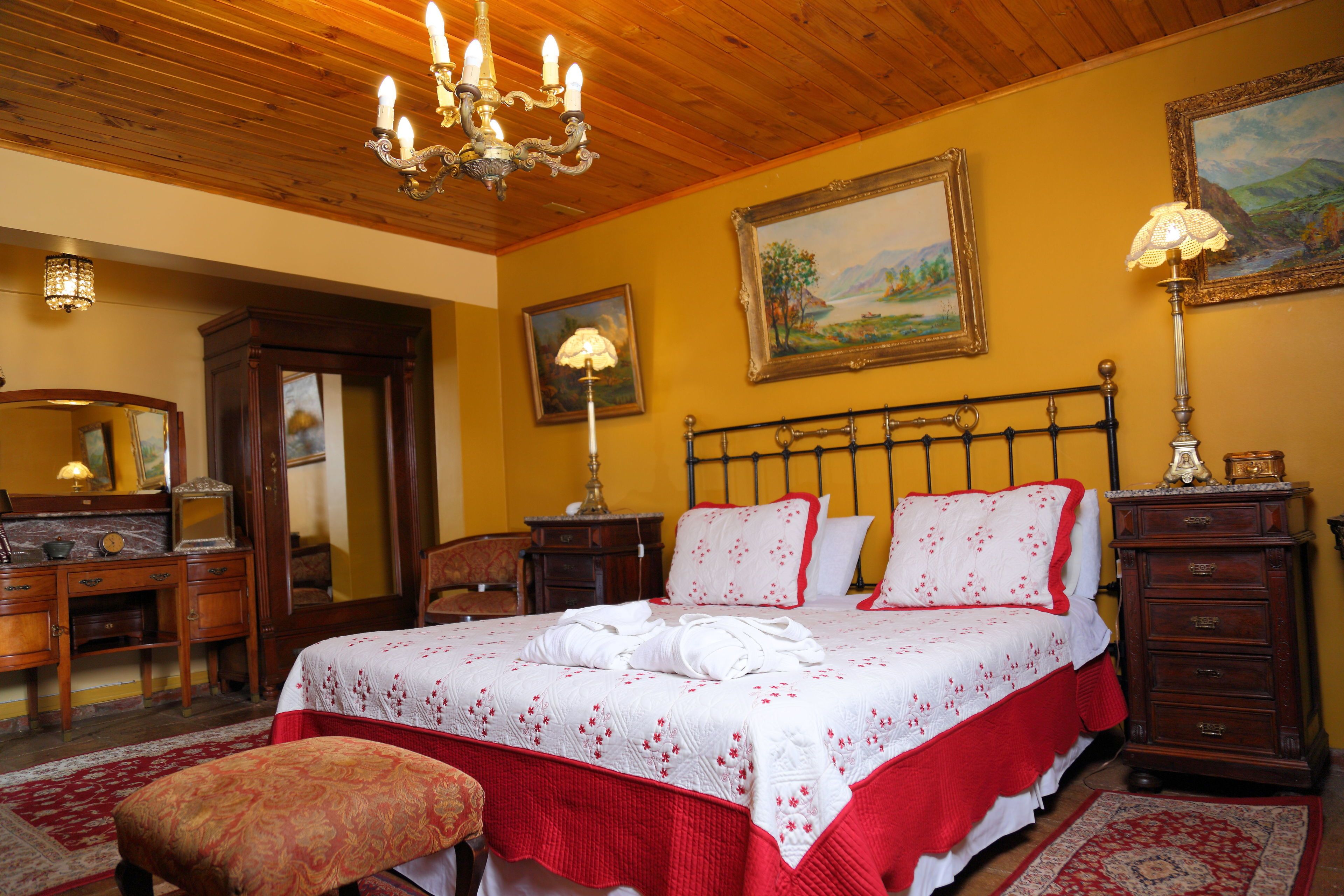 Un dormitorio bien amoblado con una cama grande, cabecera de madera, mesitas de noche, un aparador, un espejo y una araña.