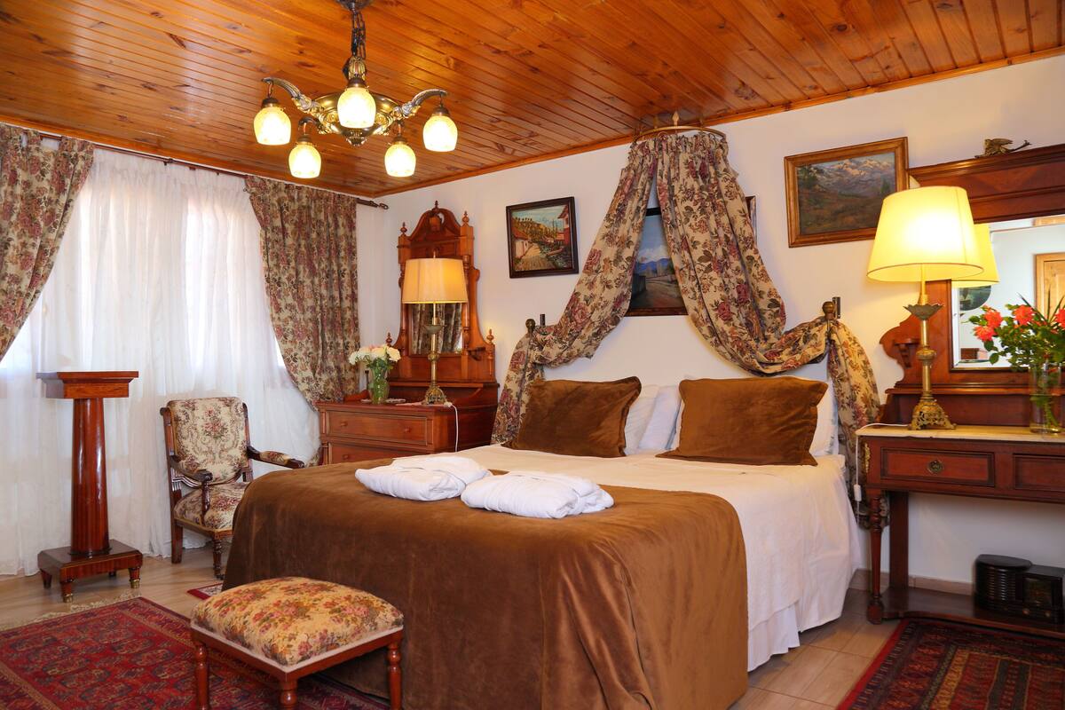 Una habitación tradicional con techo de madera, cama con ropa de cama marrón, una silla, un escritorio y una lámpara.