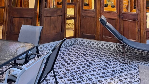 Un bâtiment en bois doté de grandes fenêtres et d’un patio couvert avec des chaises et une table.