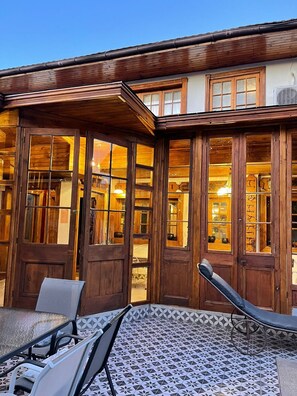 Un bâtiment en bois doté de grandes fenêtres et d’un patio couvert avec des chaises et une table.
