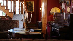 Une pièce avec un piano, une table avec des livres, un chandelier et un escalier.