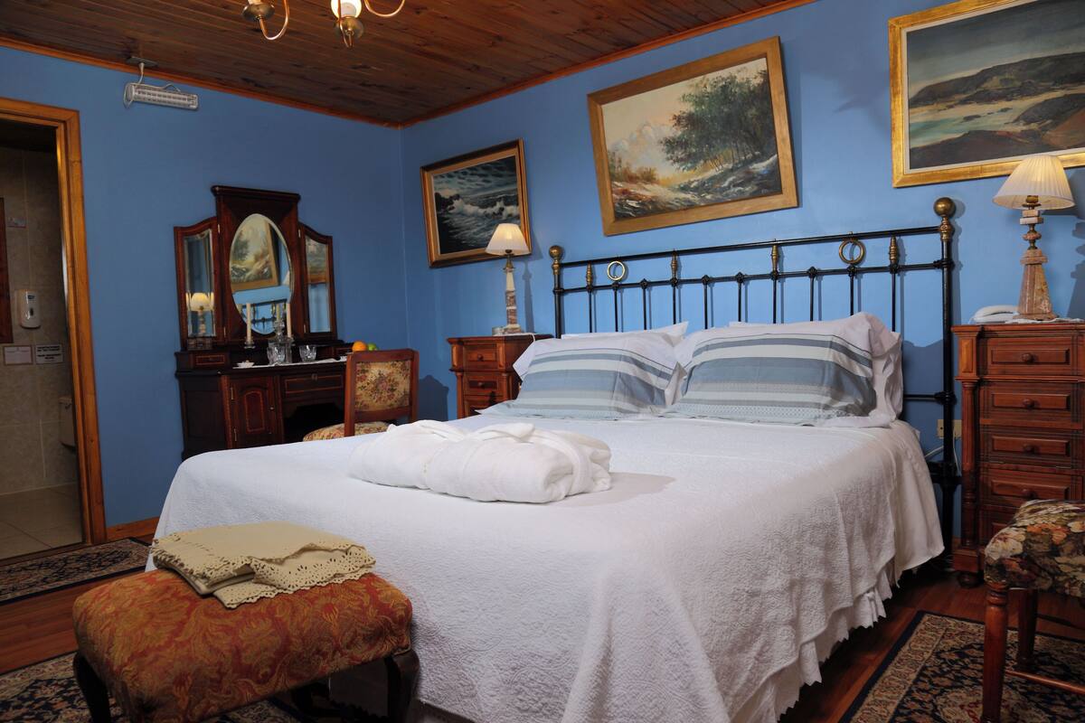 Un dormitorio ordenado con cama, un banco, cómoda y espejo.