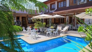 Un espace piscine agrémenté de chaises et de tables en métal blanc, entouré de plantes en pot et de parasols.
