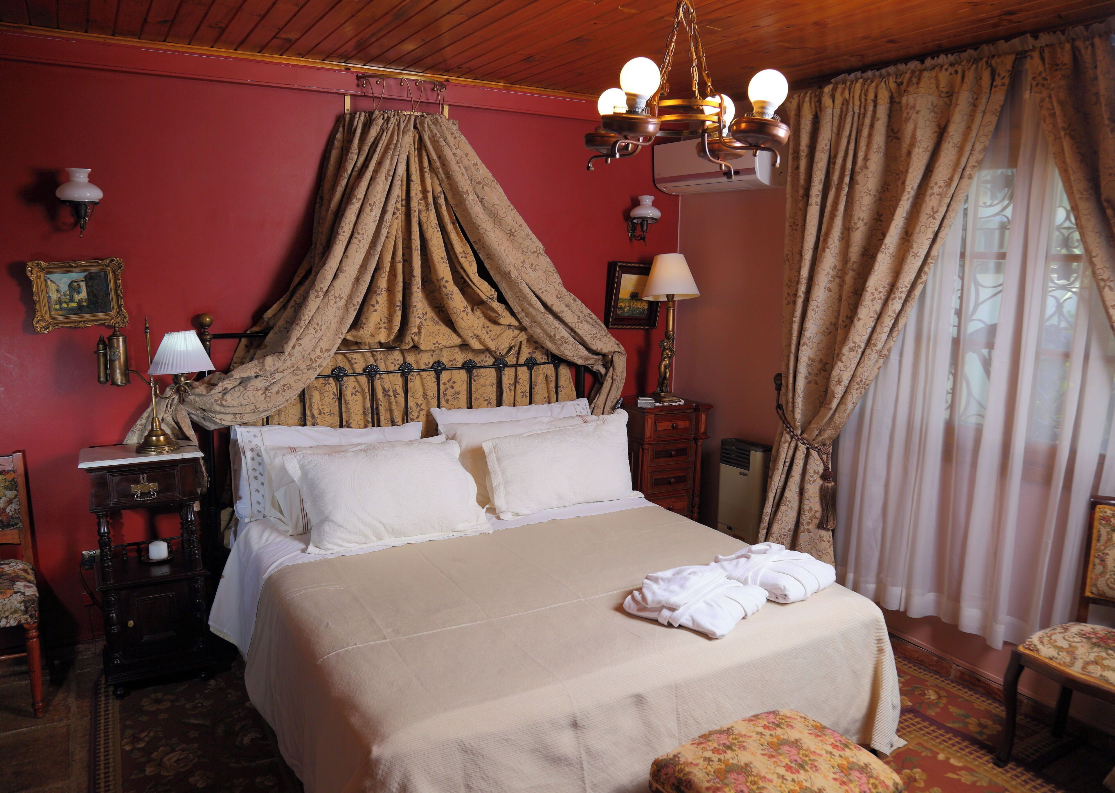 A bedroom with a four-poster bed, a chandelier, a nightstand, a dresser, and a window with curtains.