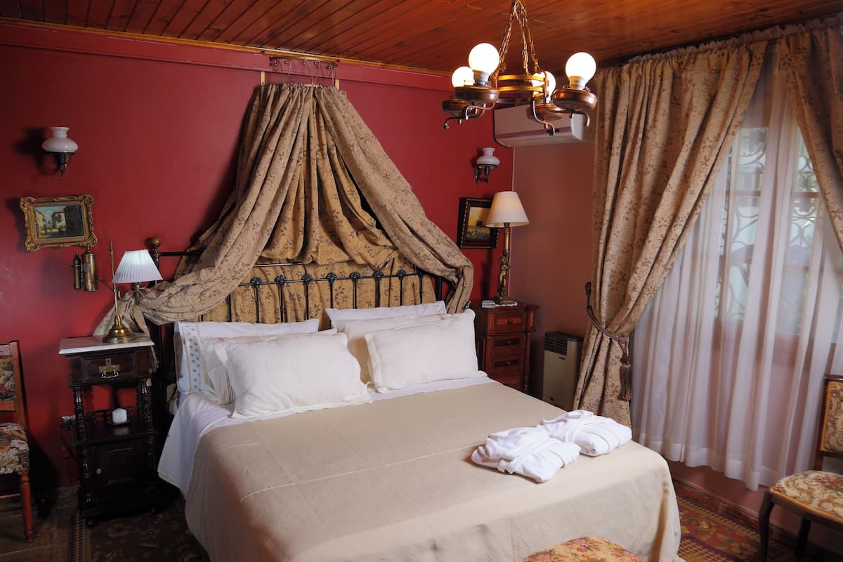 Un dormitorio con cama con dosel, candelabro, mesita de noche, cómoda y ventana con cortinas.