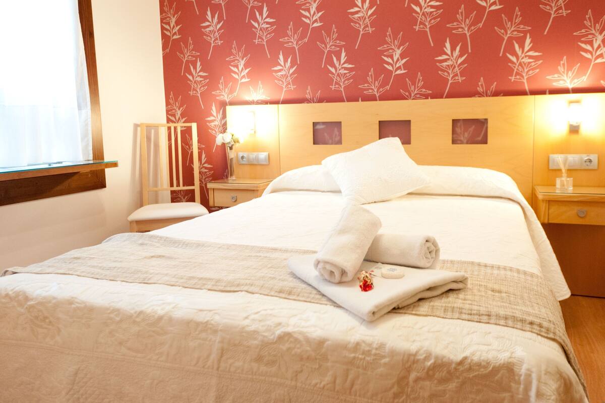 Quarto de hotel com uma cama grande, uma mesa de cabeceira com abajur e parede com padrão de folhas.