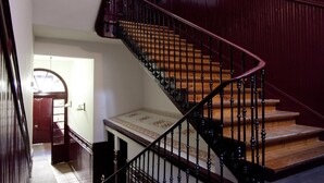 Una imponente escalera con acabado de madera y barandillas negras, que conduce a un rellano con piso estampado.