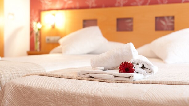 Una cama bien hecha con sábanas blancas y una decoración floral roja.