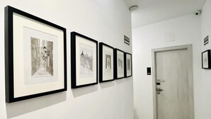 Un pasillo con fotografías en blanco y negro enmarcadas en la pared, una puerta blanca y un suelo de madera.