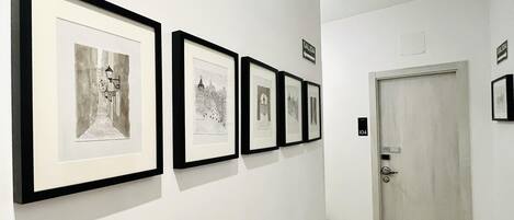 A hallway with framed black and white photographs on the wall, a white door, and a wooden floor.