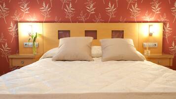 A neatly made bed with two pillows and a nightstand with a lamp and a vase of flowers.