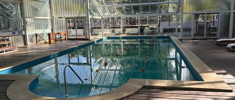Una piscina interior con cubierta de madera, paredes de vidrio y zona techada.