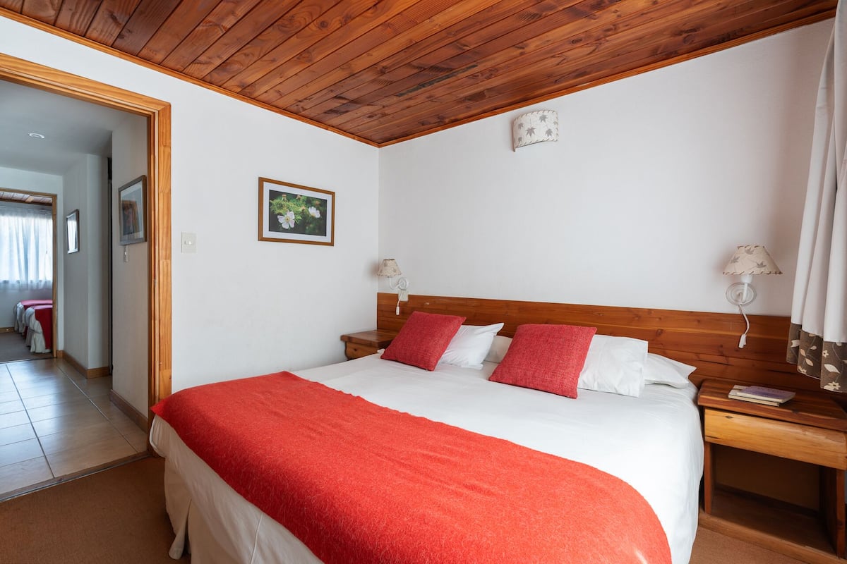 Ein Schlafzimmer mit Holzboden, einem Bett mit rot-weißer Bettwäsche, zwei Nachttischen mit Lampen und einem gerahmten Bild an der Wand.