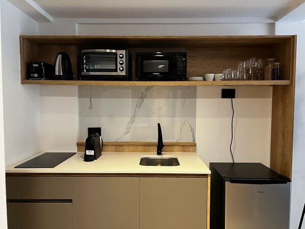 Cocina compacta con microondas, tostadora y cafetera integrados en un estante de madera.