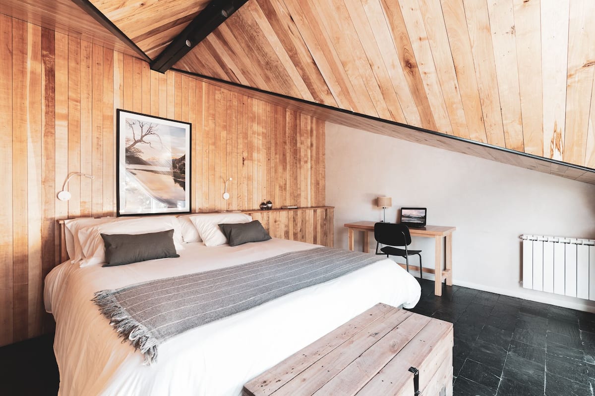 Ein Schlafzimmer mit Holzboden, einem Bett mit Kissen, einem Schreibtisch mit Stuhl und einem Heizkörper.