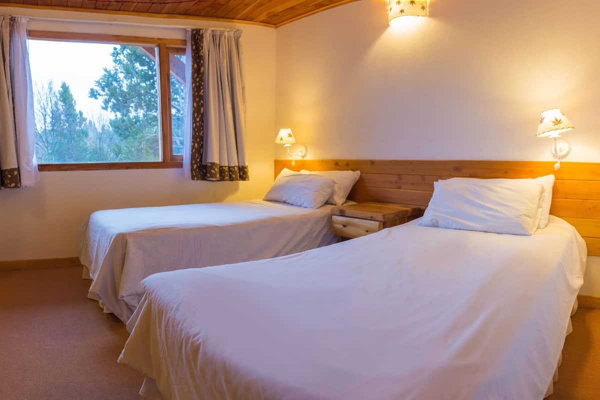 Ein Zimmer mit zwei Betten, einem Vorhangfenster und Wandlampen.