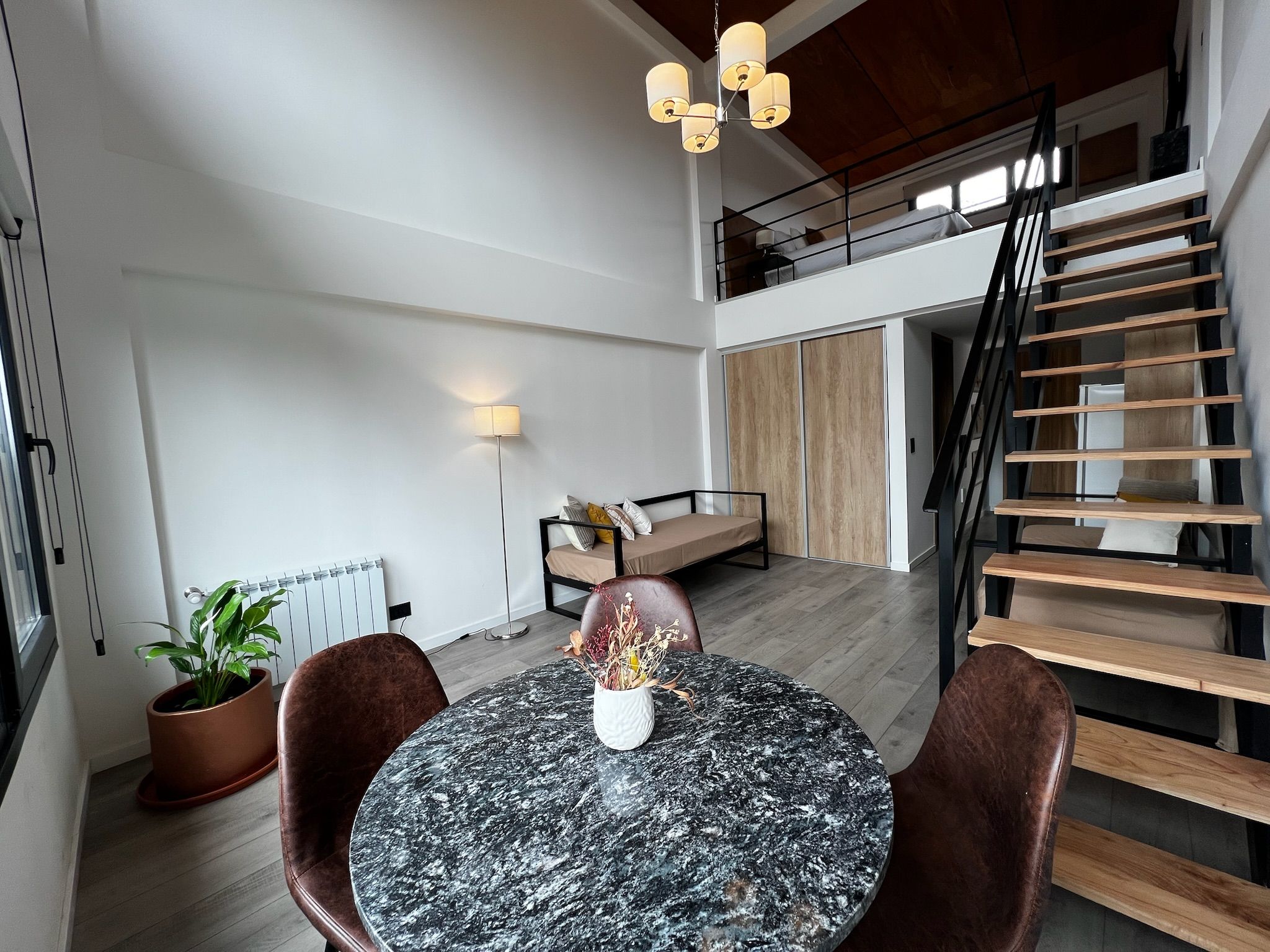 Un interior moderno con una mesa redonda de mármol, dos sillones de cuero, una planta en maceta, un sofá, una lámpara de pie y una escalera.