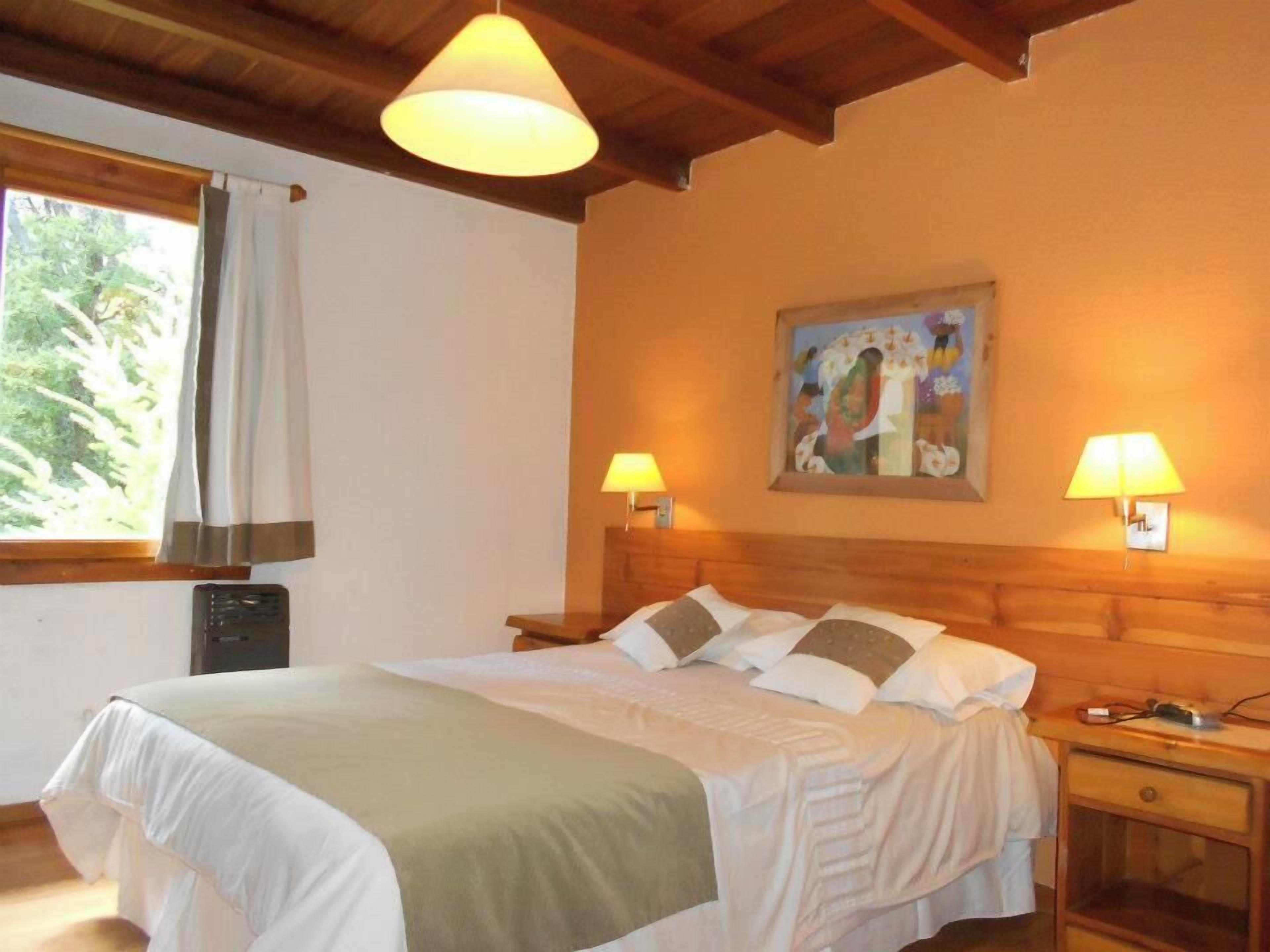 Een slaapkamer met een bed, twee bedlampen, een schilderij aan de muur en een raam met gordijnen.