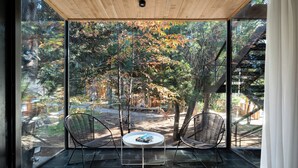 A modern room with a large glass window, two black wireframe chairs, a small round table, and a wooden ceiling.